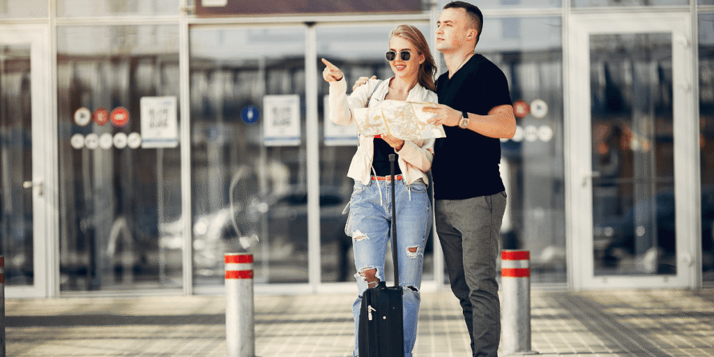 A man and woman stand with luggage in front of a building, ready for travel or check-in.