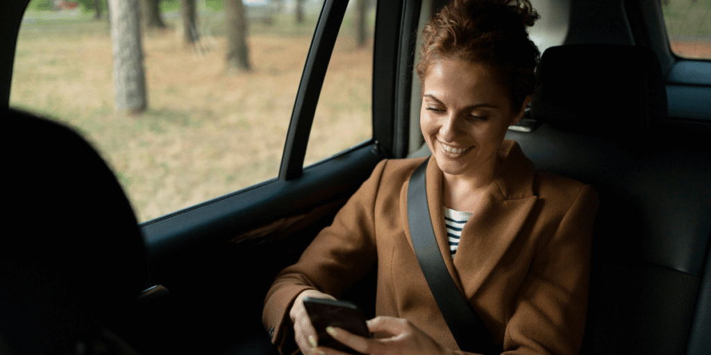 A woman in the back seat of a car, focused on her phone while seated comfortably.