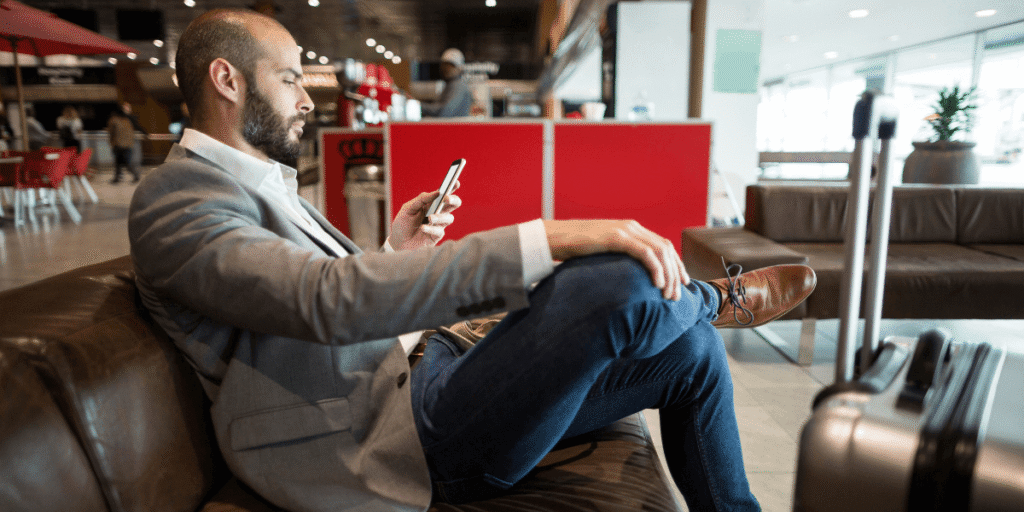 A man sitting on a couch, focused on his phone, with a relaxed expression and casual attire.