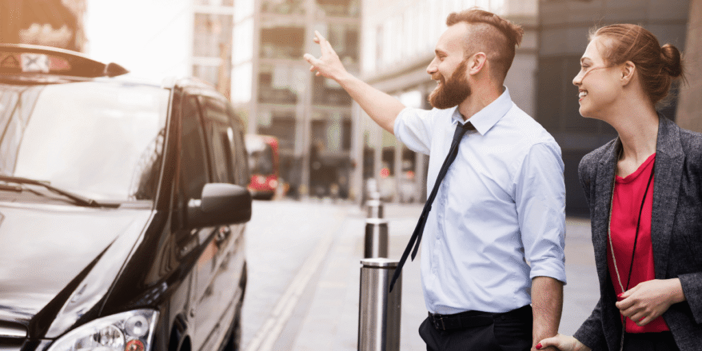 A man and woman stand beside a black car, smiling and dressed casually in a sunny outdoor setting.