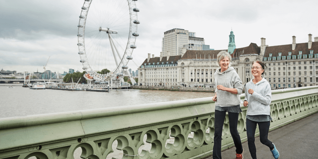 Two women jogging on a bridge with the London Eye in the background, showcasing an active urban scene.