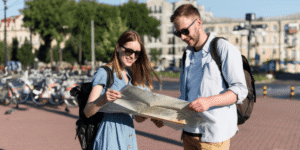Two travelers wearing sunglasses looking at a map outdoors, planning their route in a city setting.