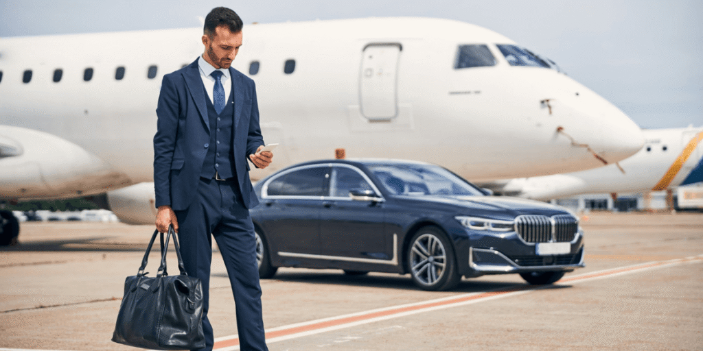 Professional man with a suitcase walking towards a luxury car at the airport.