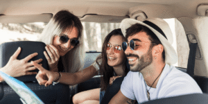 Three friends in a car share a joyful moment. A woman points at a map while others smile, wearing sunglasses. The mood is playful and adventurous.
