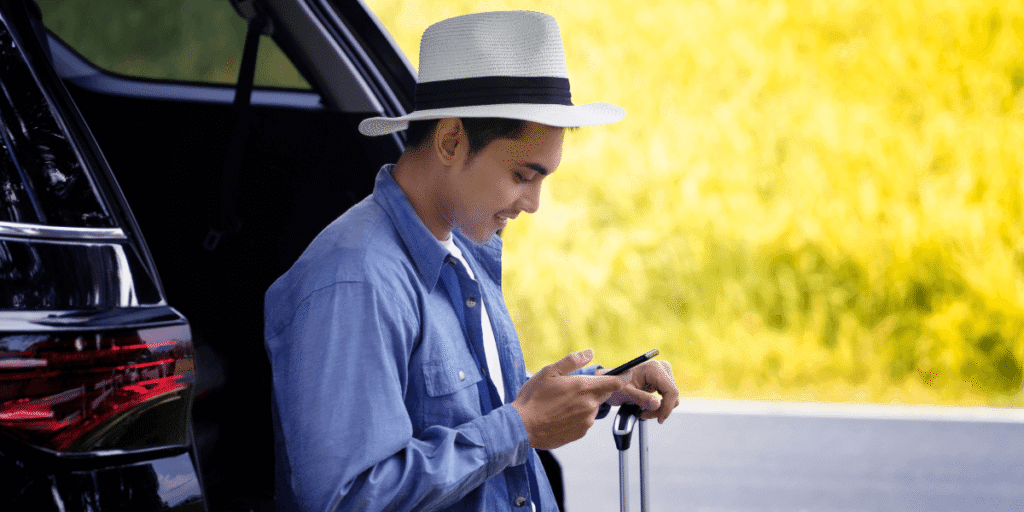 A man wearing a hat sits in the back seat of a car, looking out the window with a thoughtful expression.