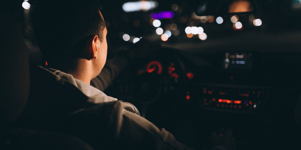 Personal Safety Tips for Any Late-Night Journey (1) A man driving a car at night, illuminated by the vehicle's headlights.
