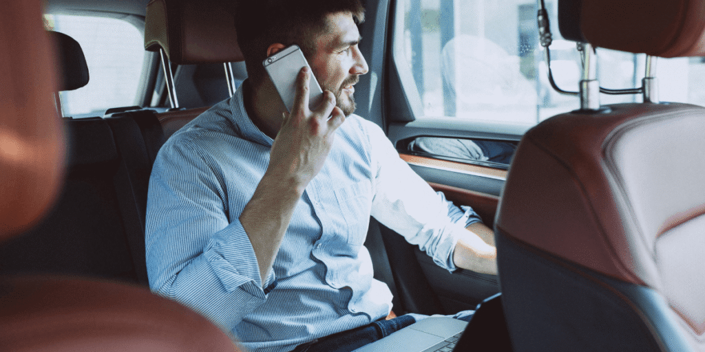 A man seated in the back of a car, engaged in a conversation on his cell phone.