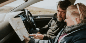 A man and woman in a car, focused on a map, planning their route together.