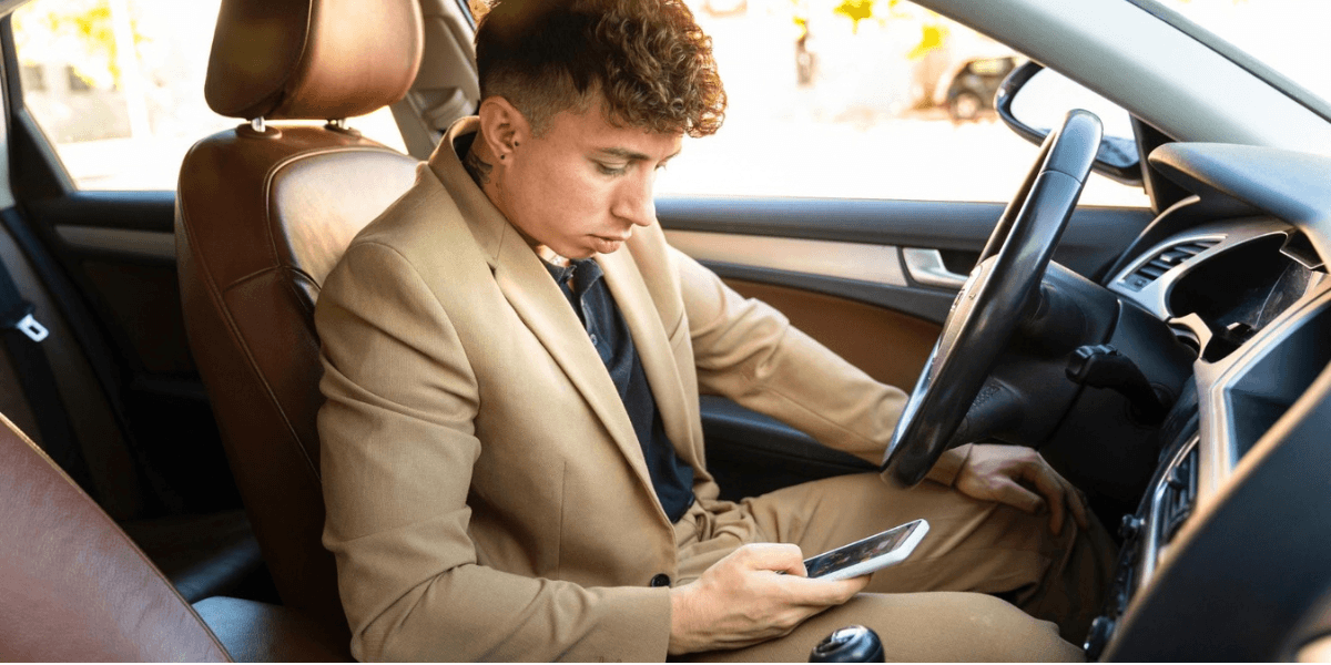 A man in a suit seated in the driver's seat of a car, focused on the road ahead.