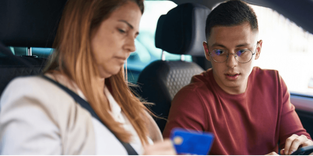 A man and woman in a car examine a credit card, appearing engaged in a financial discussion.